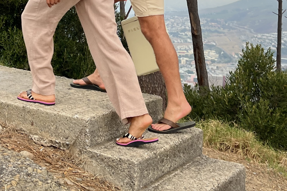 Two people climbing up concrete steps in leather flip flops with a scenic background of trees and mountains.