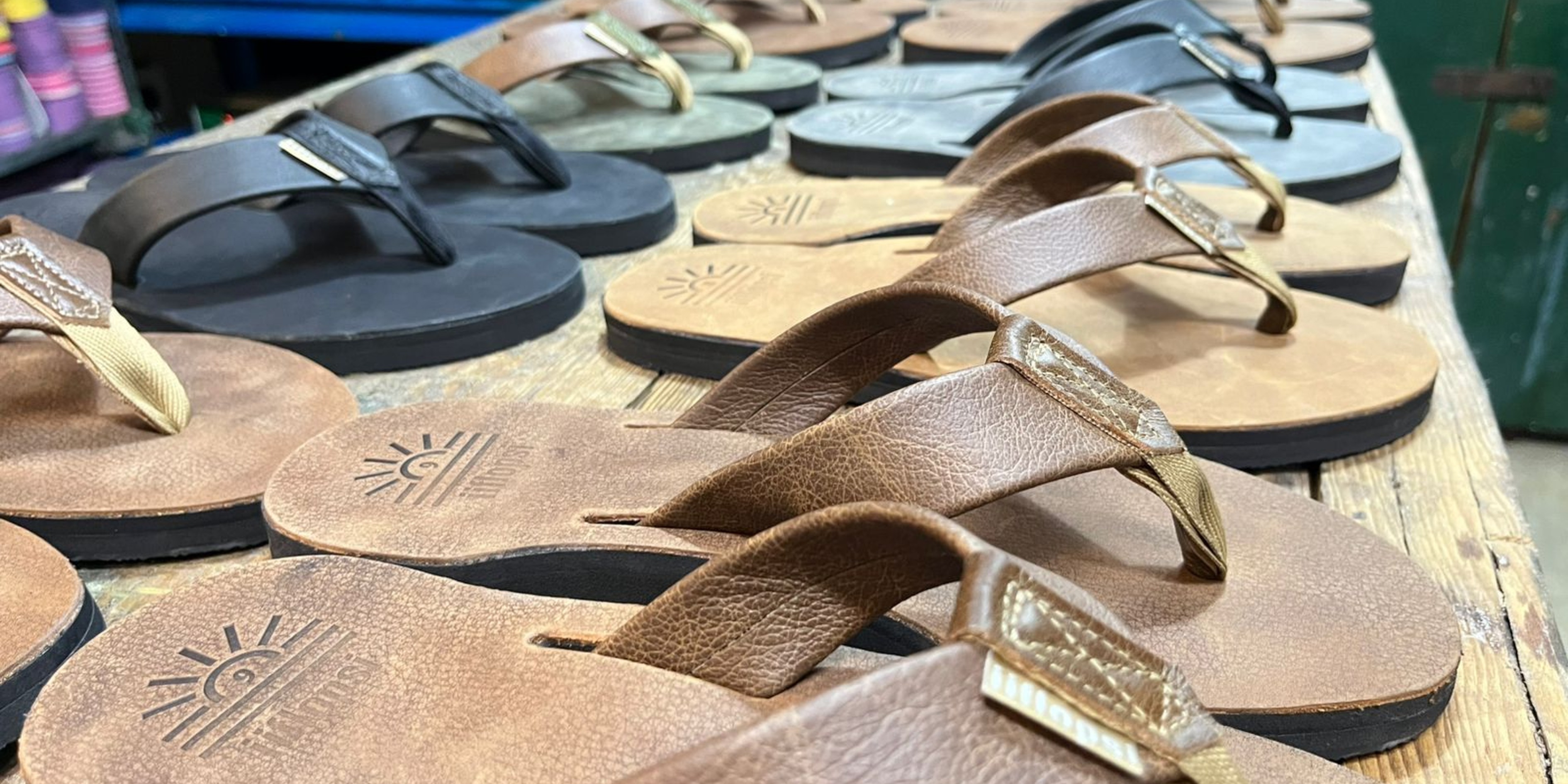 Row of handmade leather flip flops on a wooden surface with various colours.